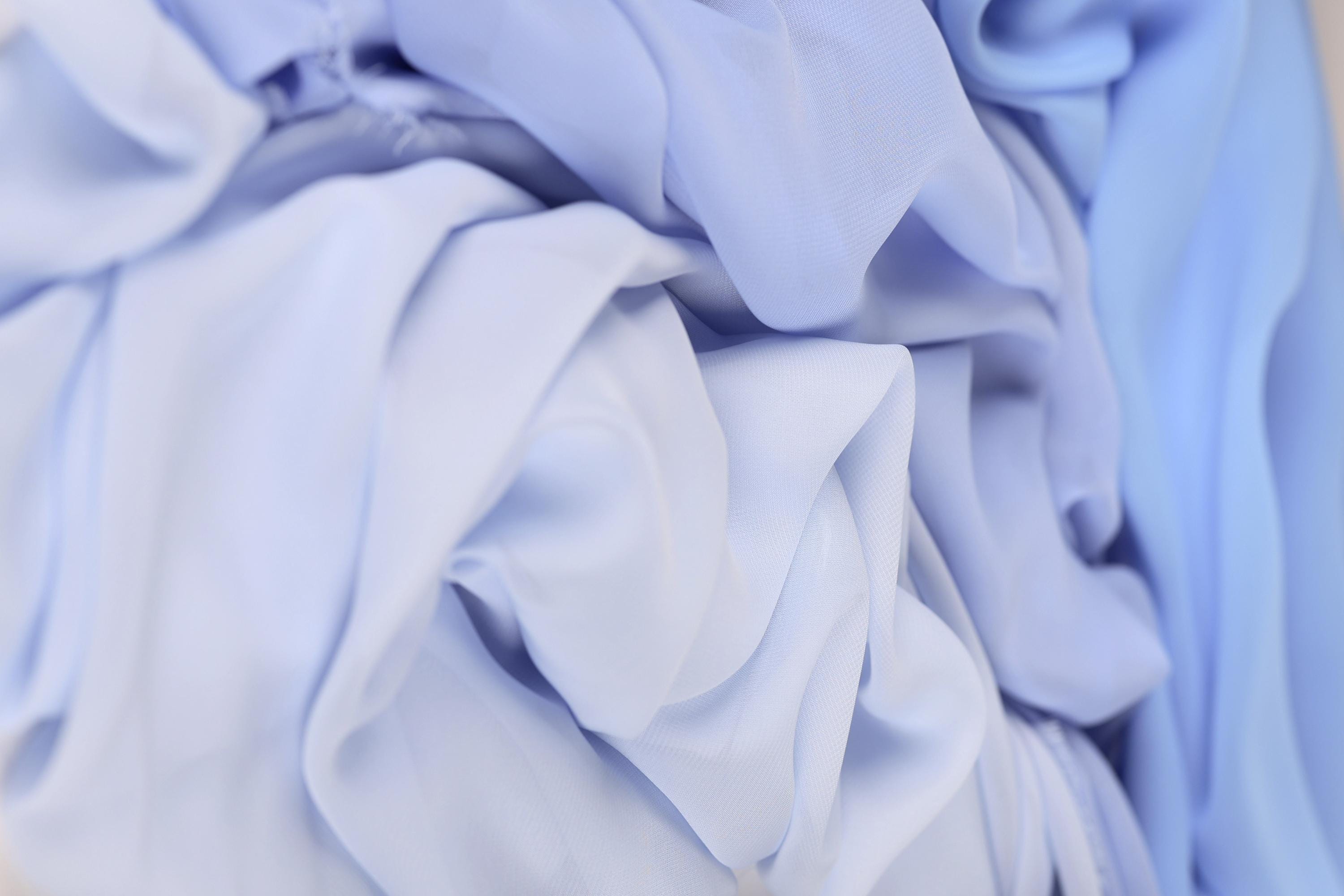 The image is a close-up of a crumpled, light blue fabric, with a blurred background.