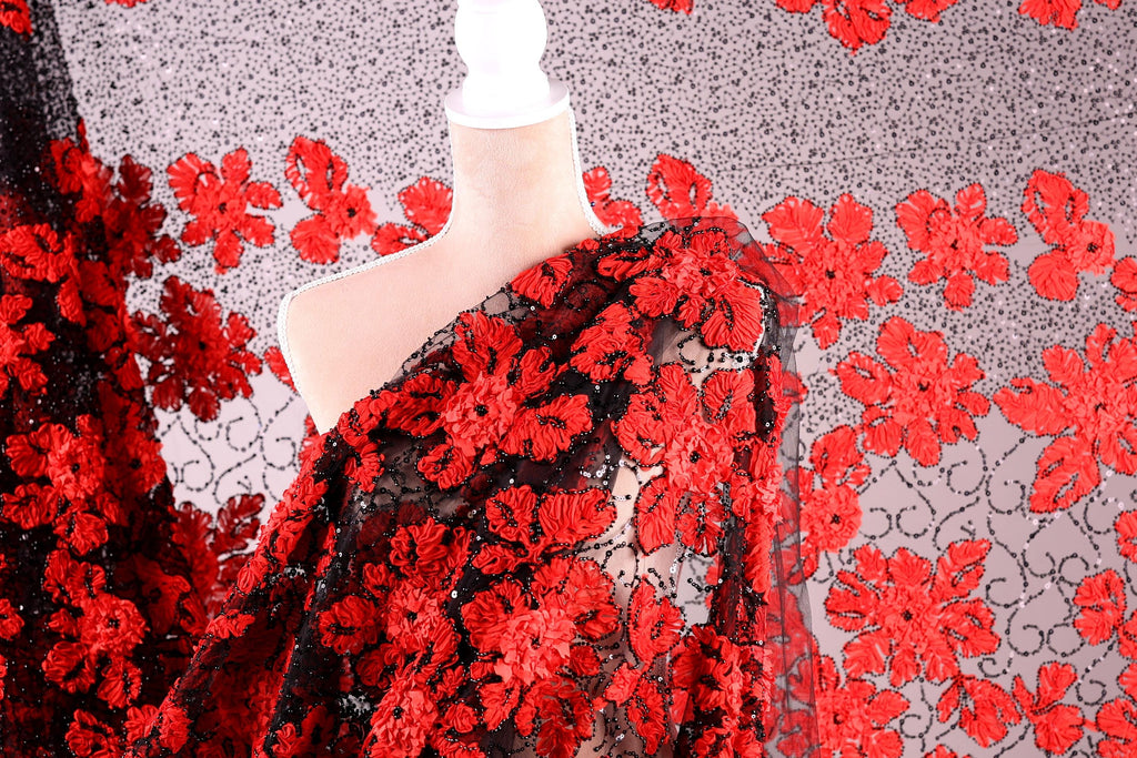 a mannequin wearing a red and black floral print dress. The dress has a black bodice with a red floral pattern, and the fabric appears to be sheer, allowing the red flowers to be visible. The background is a gray and white patterned fabric with red flowers.