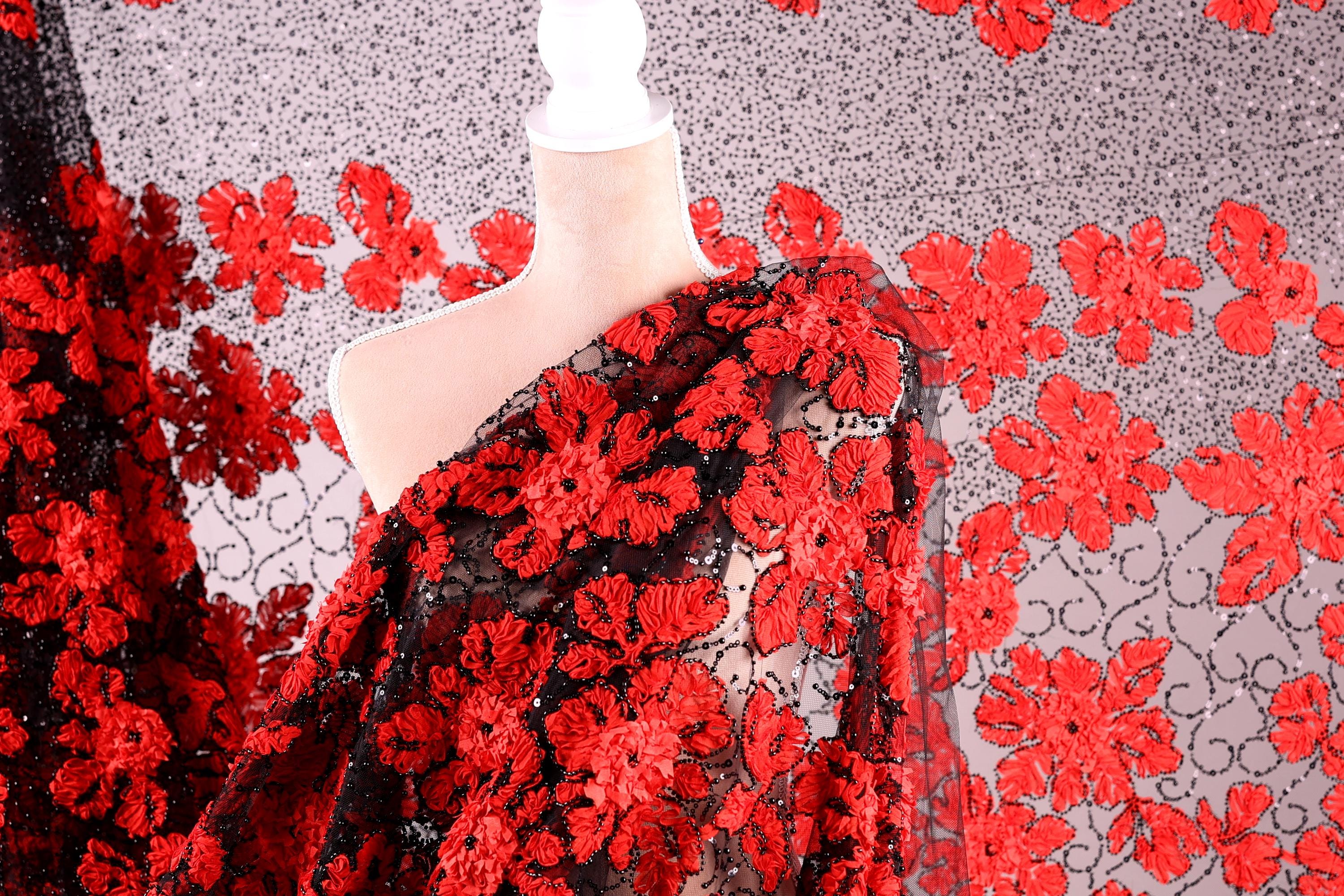 a mannequin wearing a red and black floral print dress. The dress has a black bodice with a red floral pattern, and the fabric appears to be sheer, allowing the red flowers to be visible. The background is a gray and white patterned fabric with red flowers.