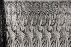 a close-up view of a black and white patterned fabric with a repeating floral design. The pattern consists of long, thin lines that create a sense of movement and rhythm across the fabric. The design is intricate and detailed, with each line contributing to the overall visual impact of the pattern.