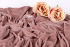 Two light pink roses resting on a crumpled pink velvet fabric.