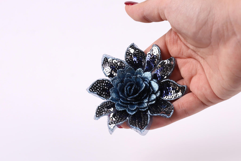 A hand holding a blue sequin flower against a white background.