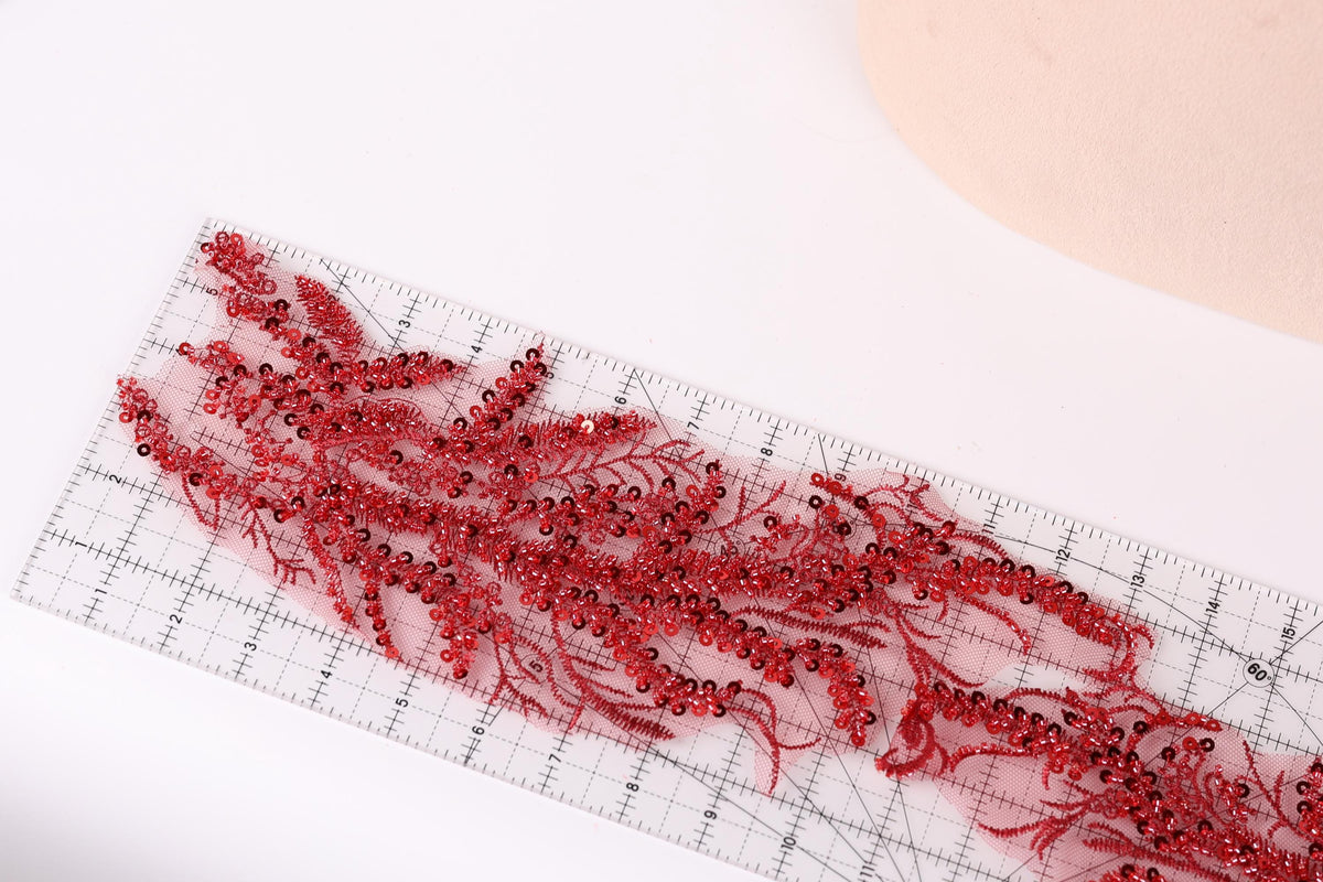 a clear ruler with red sequin beads arranged on it, placed on a white surface.
