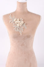 A mannequin wearing a beige dress with a delicate floral embroidered patch on the shoulder.