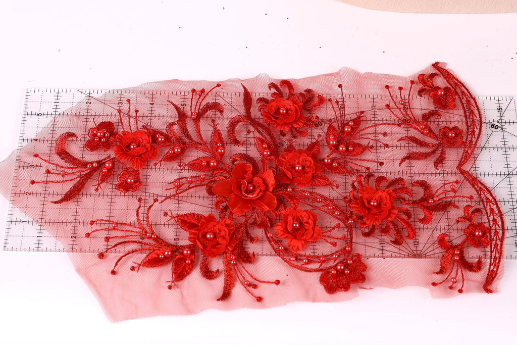 a close-up view of a red floral embroidery design on a white background. The design consists of numerous red flowers with intricate details, including petals and beads, arranged in a visually appealing manner. The flowers are spread across the image, creating a vibrant and eye-catching display.