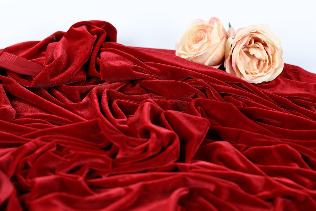 two roses resting on a crumpled red velvet fabric.