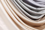 A close-up view of a pile of fabric, with a gradient of colors ranging from light to dark shades of gray and beige.