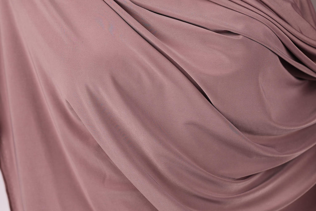 a close-up view of a soft, flowing fabric in a deep pink color. The fabric appears to be made of silk or a similar material, with a smooth and shiny texture. The fabric is draped or folded in a way that creates a sense of movement and softness.