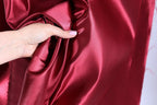 A hand is holding a piece of red satin fabric, with the fabric partially draped over the hand.