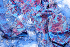 The image is a close-up of a fabric with a vibrant blue and red pattern, featuring intricate designs and sparkling embellishments.
