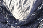 a close-up view of a fabric with a dark blue, sequined pattern. The fabric appears to be made of a sheer material, with a delicate and intricate design featuring small sequins and beads. The background is blurred, drawing focus to the fabric and its details.