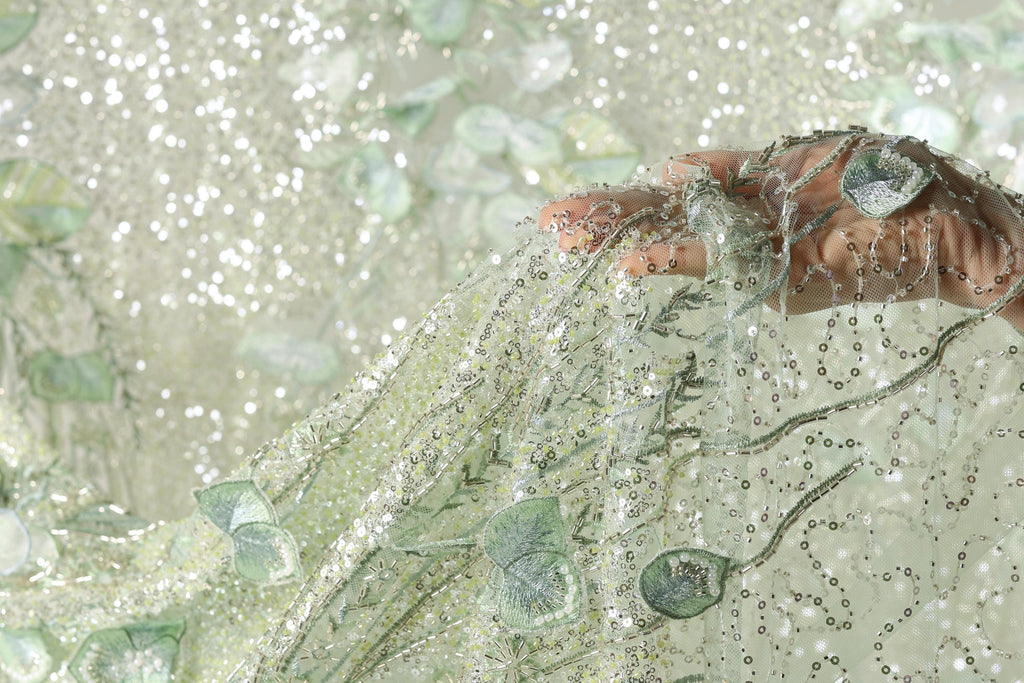 A hand is holding a piece of fabric with a delicate, shimmering green and white pattern.