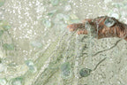 A hand is holding a piece of fabric with a delicate, shimmering green and white pattern.