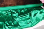 a close-up view of a crumpled, shiny green fabric, possibly silk or satin, with a dark background.