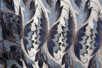 a close-up view of a fabric with a repeating pattern of blue and white flowers or leaves, with some areas of the fabric appearing to be sequined or adorned with glitter.