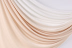 a close-up view of a fabric with a gradient of colors, transitioning from light to dark shades of peach and white. The fabric appears to be made of silk or a similar material, and it is draped or folded in a way that creates a sense of movement and texture. The colors are vibrant and the fabric looks soft and luxurious.