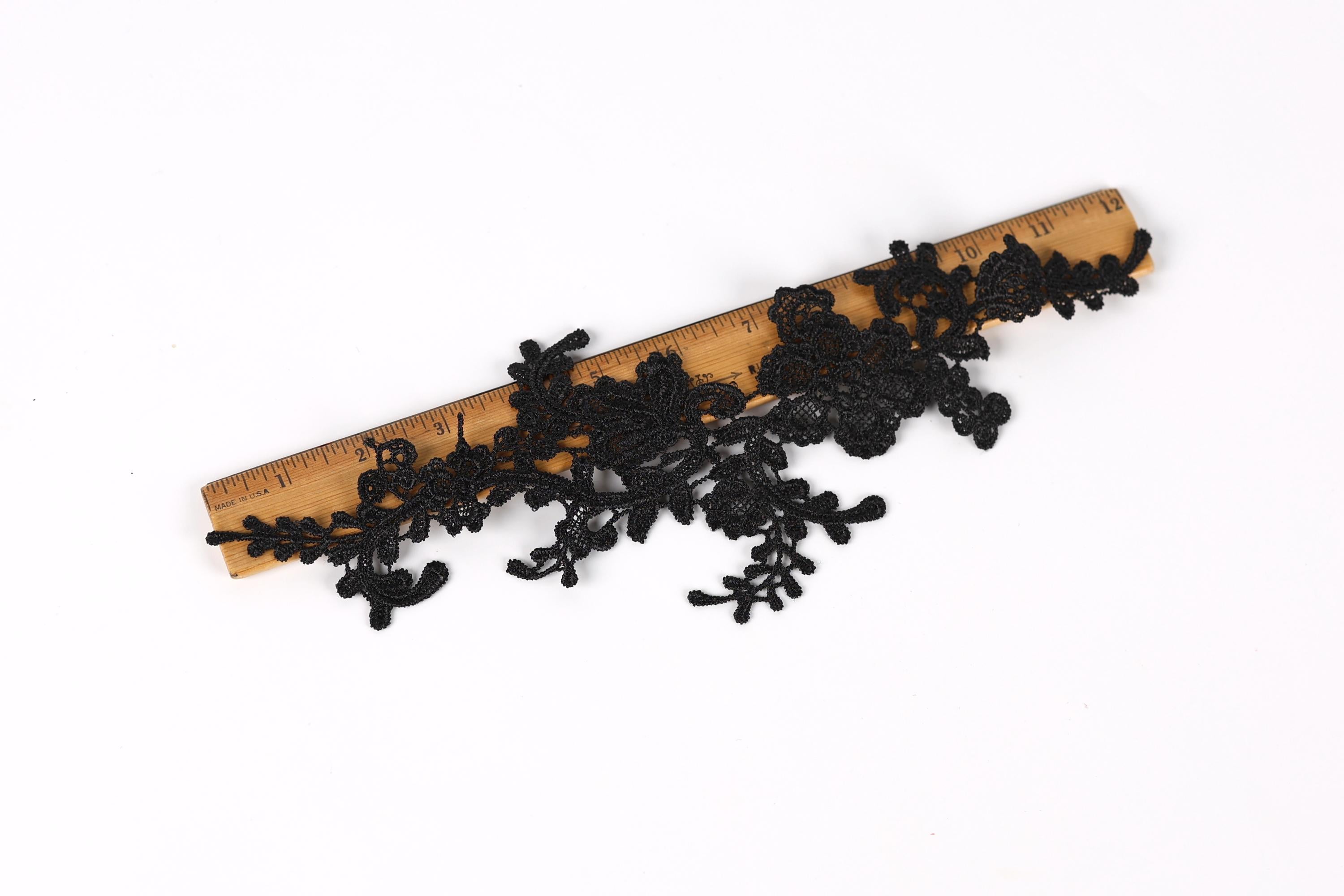 a piece of black lace or fabric with intricate floral patterns, placed on top of a wooden ruler.