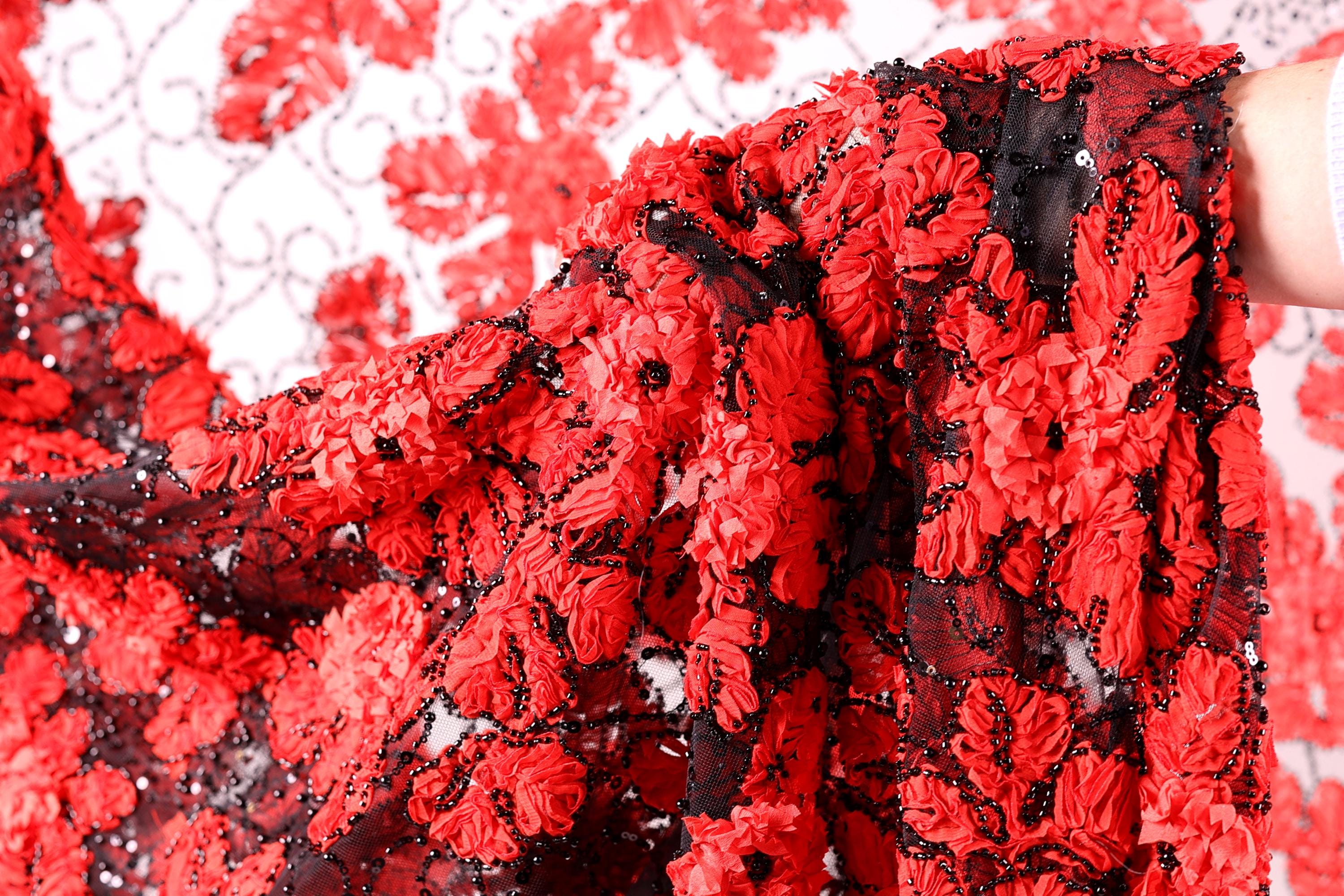 a close-up view of a fabric with a striking red and black floral pattern. The fabric appears to be made of a sheer material, with a black lace-like texture that adds an elegant touch. The close-up perspective allows for a detailed examination of the intricate design and the vibrant colors of the fabric.