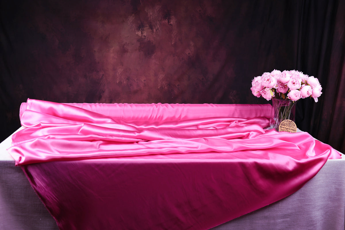 a pink satin tablecloth draped over a table, with a vase of pink flowers placed on it.