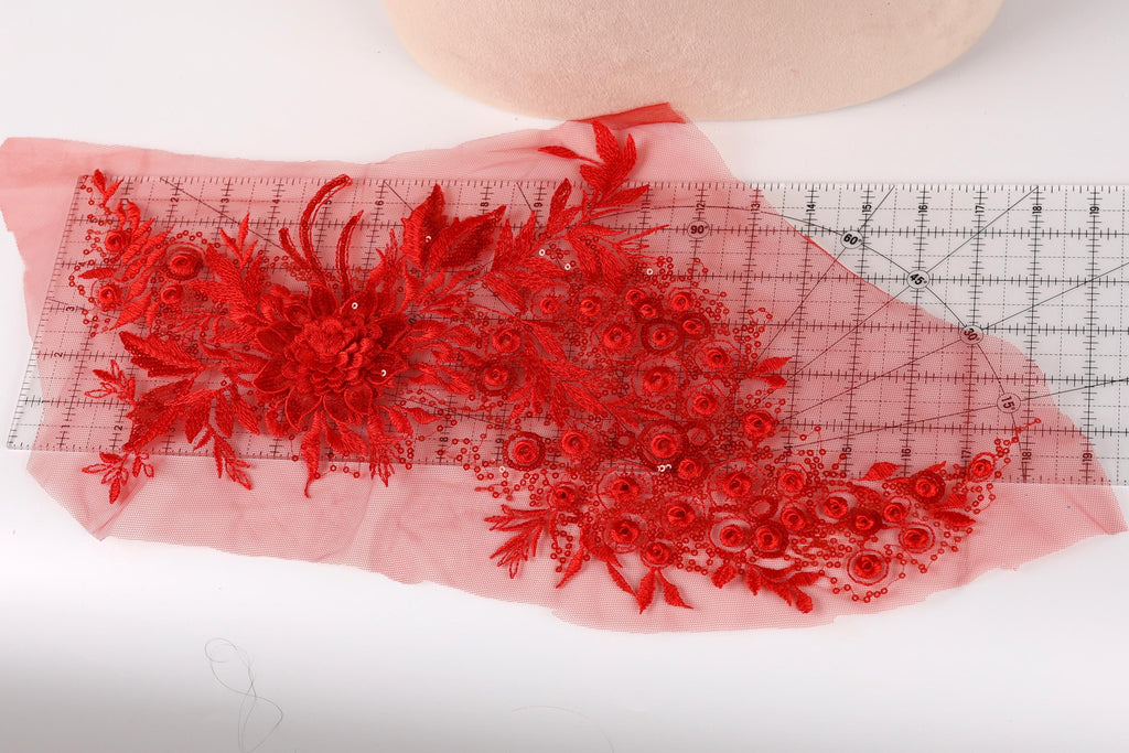 a close-up view of a red floral embroidery on a piece of fabric, with a ruler placed next to it.
