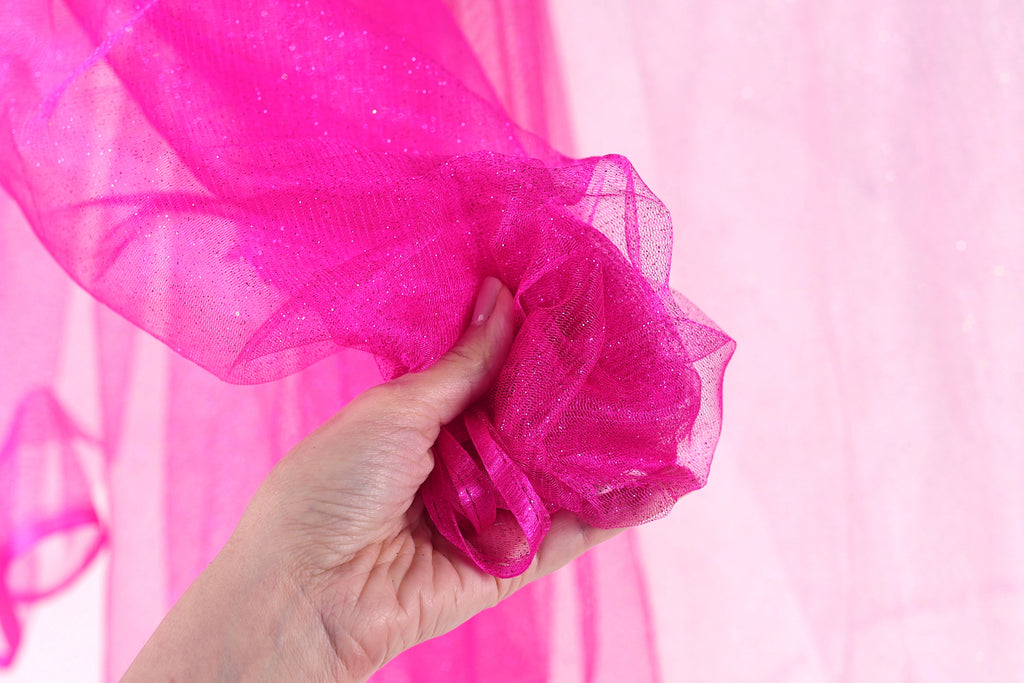 A hand is holding a pink, shiny fabric against a pink background.