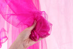 A hand is holding a pink, shiny fabric against a pink background.