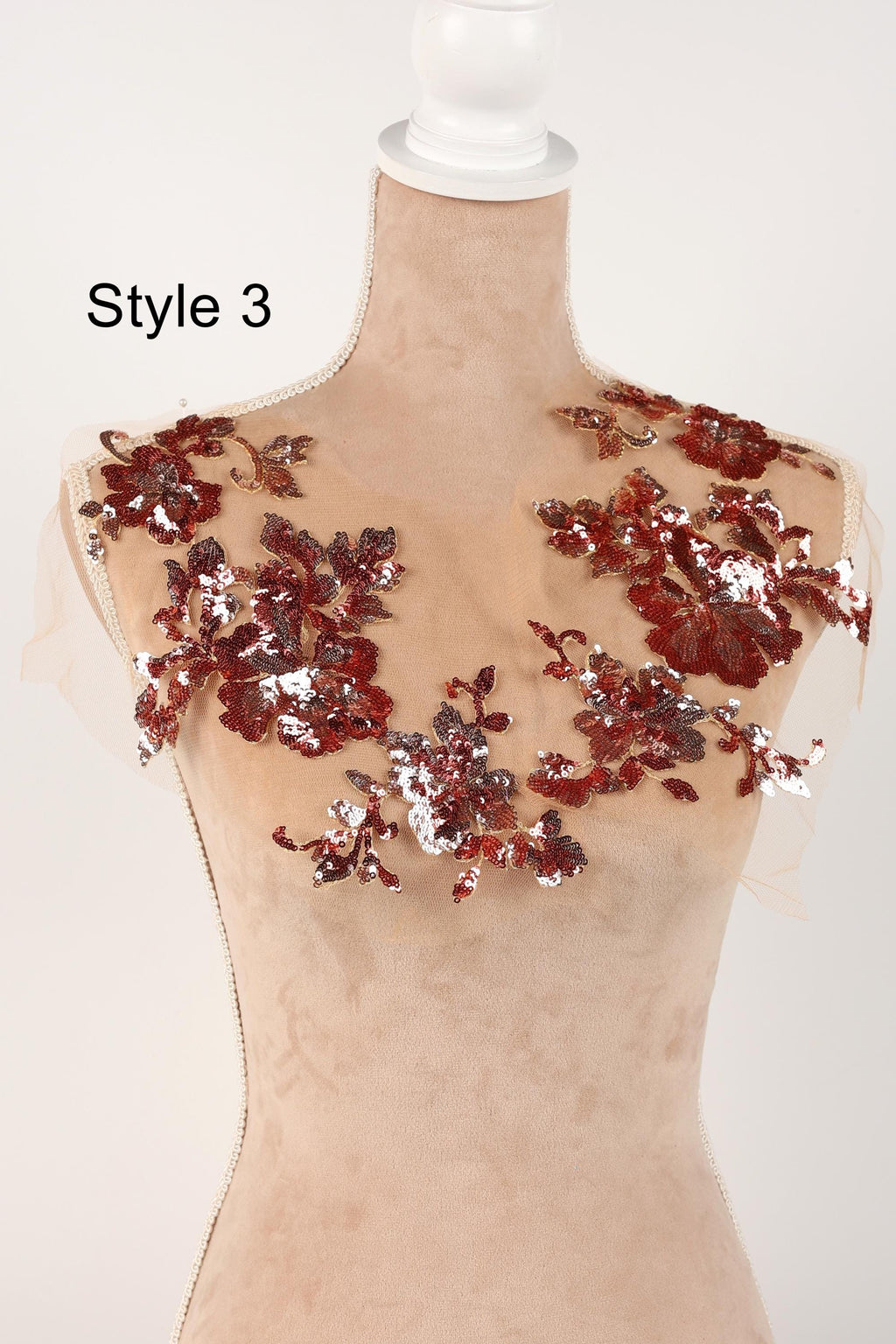 A mannequin wearing a beige dress with red and silver sequin details on the shoulders and neckline.