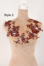A mannequin wearing a beige dress with red and silver sequin details on the shoulders and neckline.