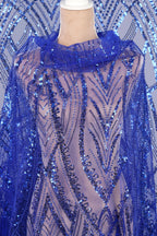 a mannequin wearing a dress with a blue sequin pattern. The dress has a sheer, flowy design with a high collar and long sleeves, giving it a dramatic and elegant appearance.