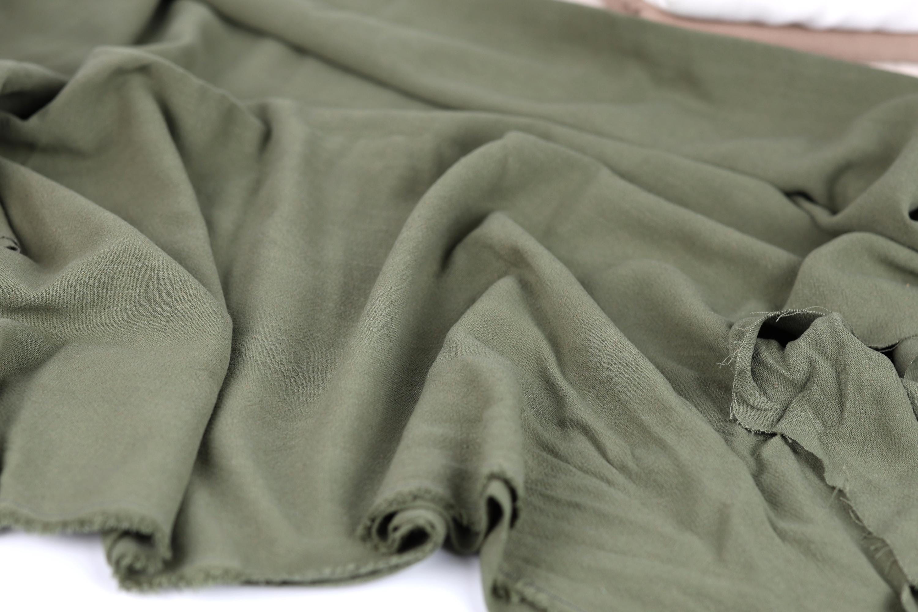 A close-up view of a crumpled, olive green fabric, possibly a piece of clothing or textile.