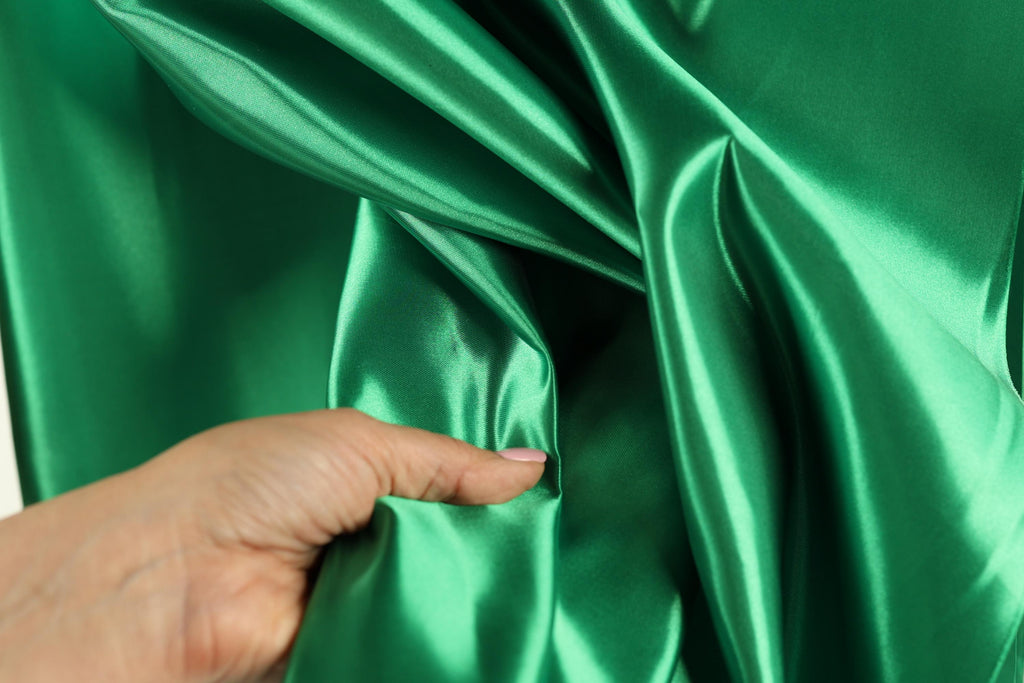 A hand is holding a piece of green satin fabric, examining its texture and appearance.