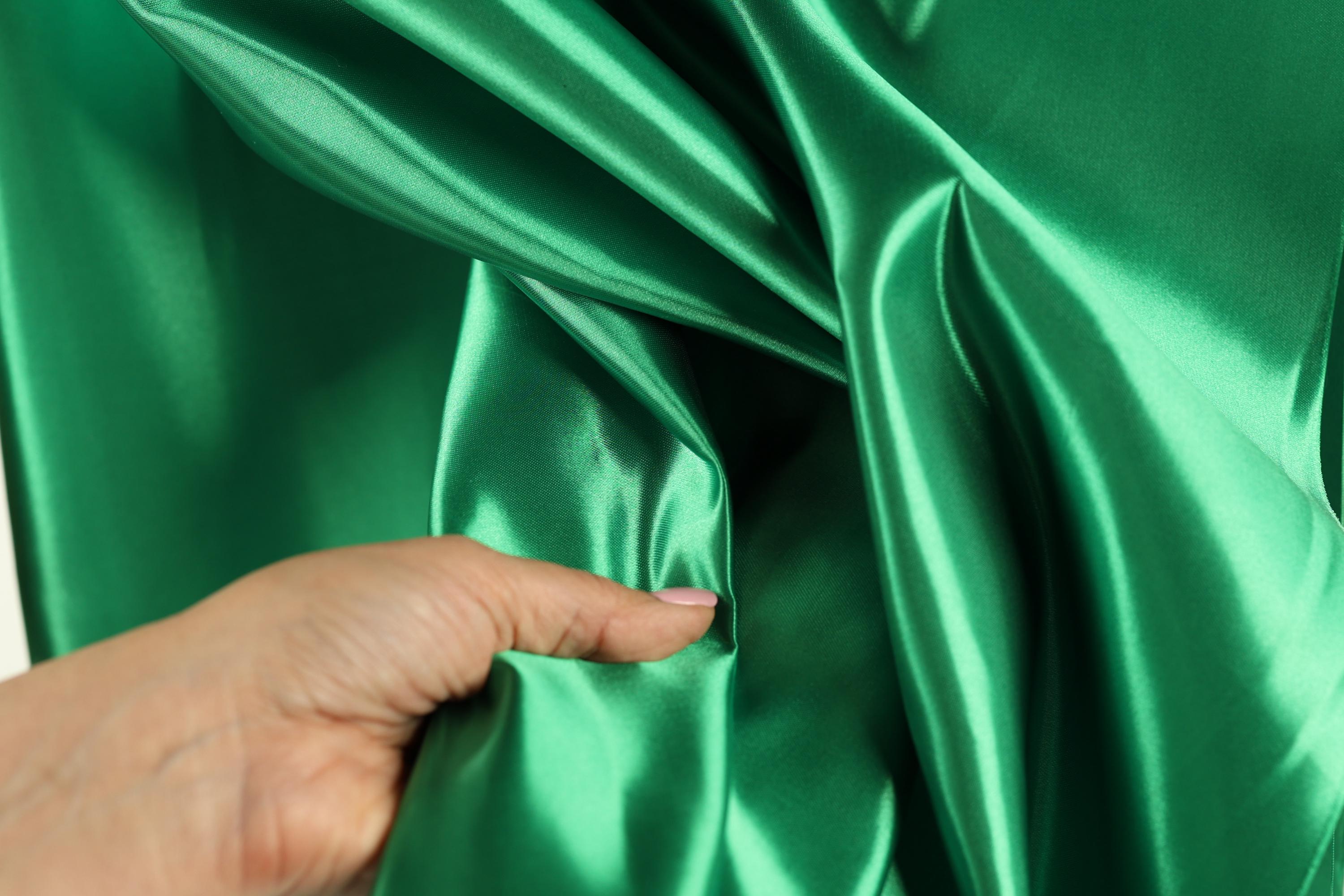 A hand is holding a piece of green satin fabric, examining its texture and appearance.