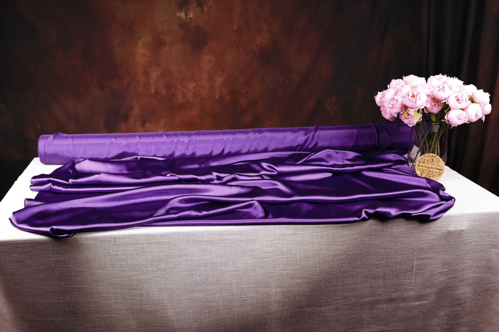 a purple fabric draped over a table, with a vase of pink flowers placed next to it.
