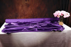 a purple fabric draped over a table, with a vase of pink flowers placed next to it.