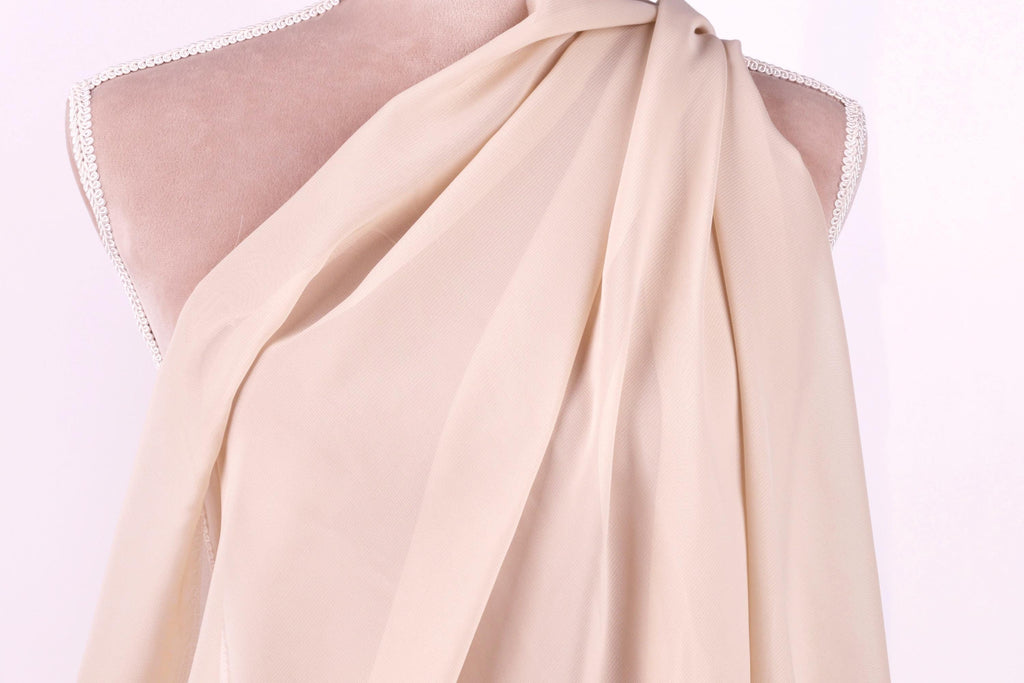 A mannequin wearing a light pink, draped fabric draped over its shoulder.