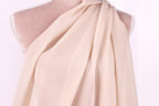 A mannequin wearing a light pink, draped fabric draped over its shoulder.
