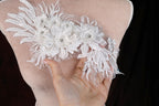 A hand is holding up a delicate, white lace flower embellishment on a dress form.