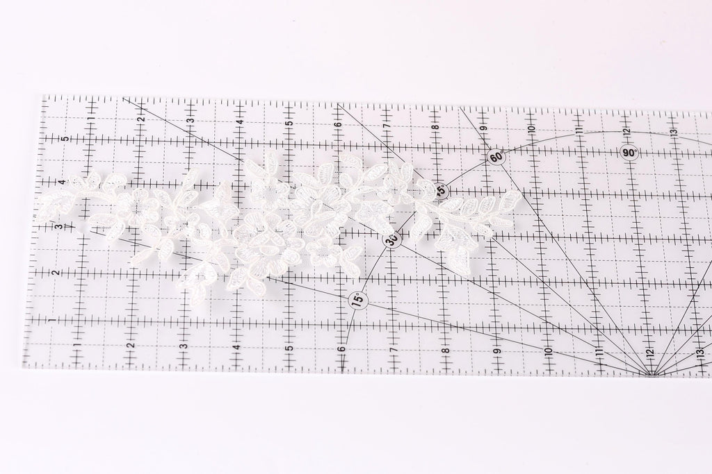 a clear ruler with a grid pattern, and there are several white lace pieces placed on the ruler.