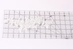 a clear ruler with a grid pattern, and there are several white lace pieces placed on the ruler.