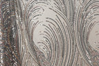 a close-up view of a fabric with a repeating pattern of sequin designs. The sequins appear in various shades of gray, black, and silver, creating a visually striking and intricate design. The fabric has a textured appearance, with the sequins adding depth and dimension to the overall pattern.