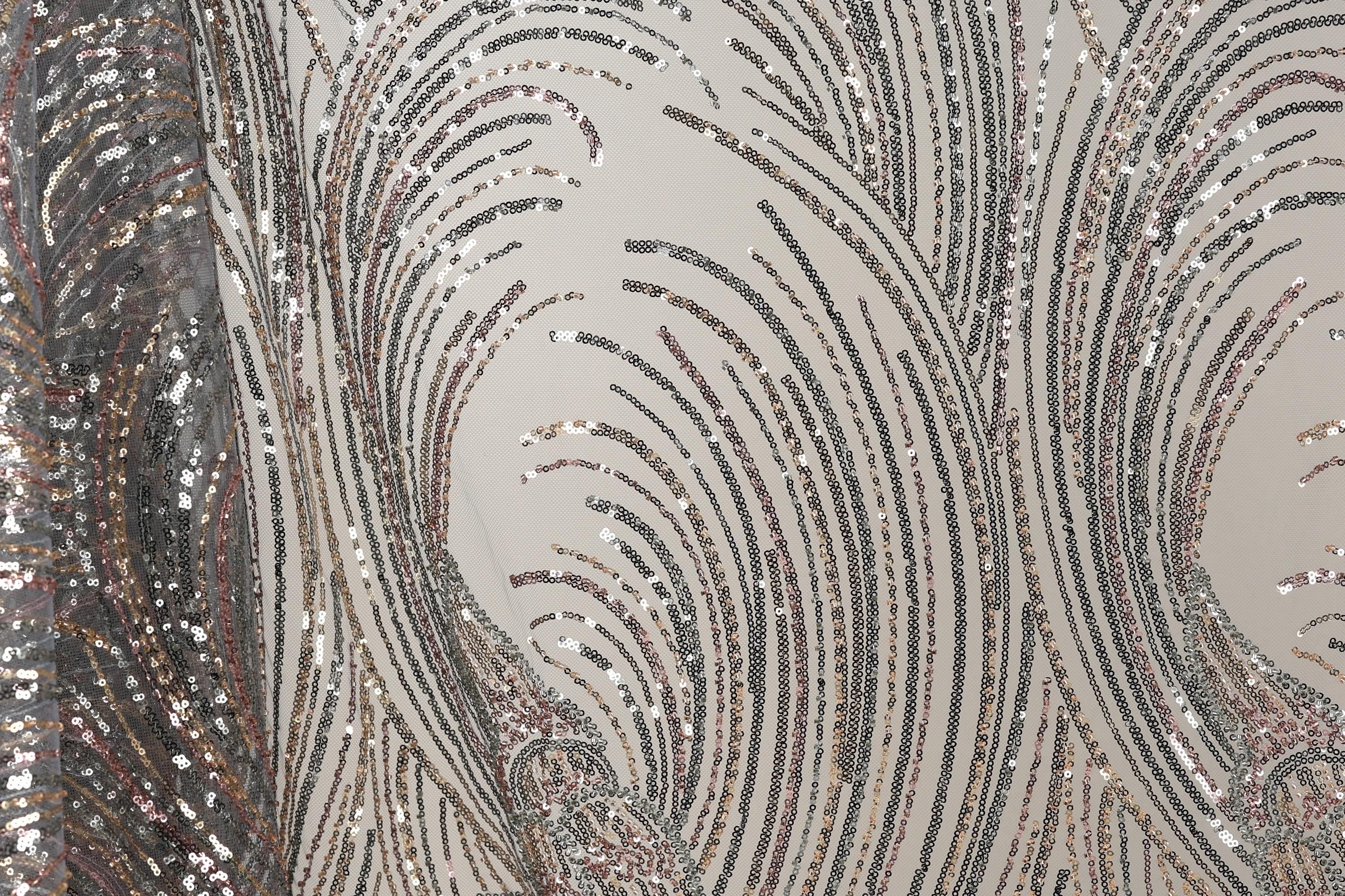 a close-up view of a fabric with a repeating pattern of sequin designs. The sequins appear in various shades of gray, black, and silver, creating a visually striking and intricate design. The fabric has a textured appearance, with the sequins adding depth and dimension to the overall pattern.