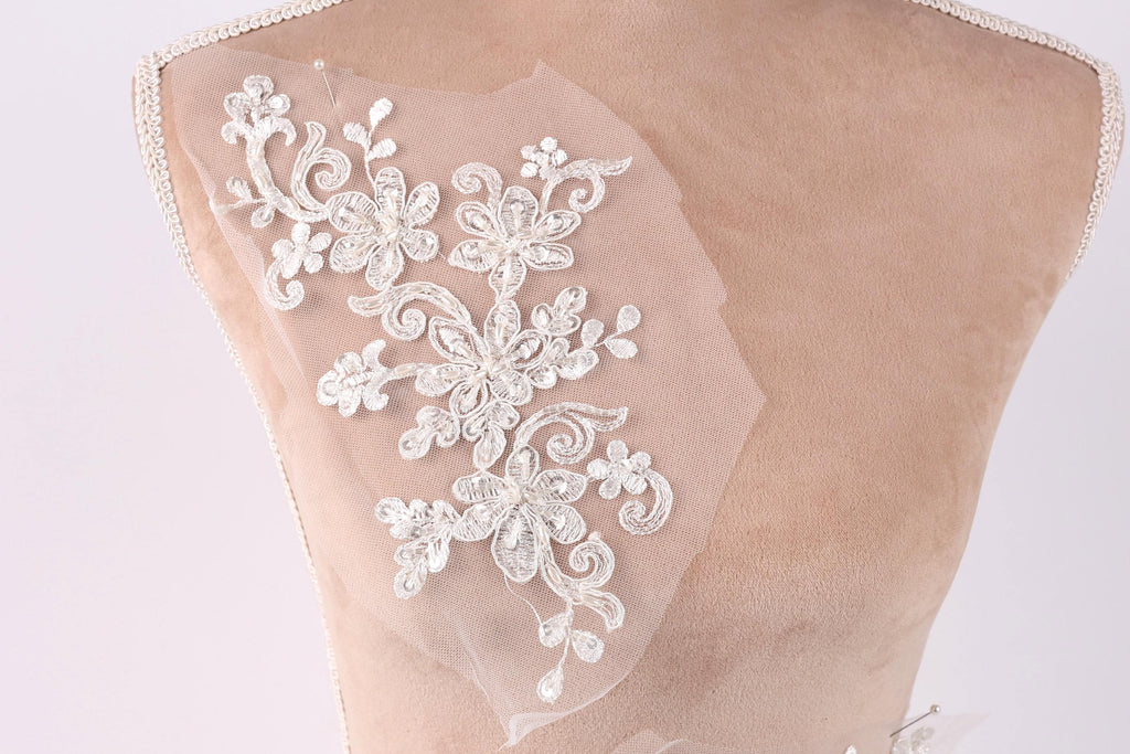 A close-up of a mannequin torso with a delicate, intricate white lace embroidery on the back.