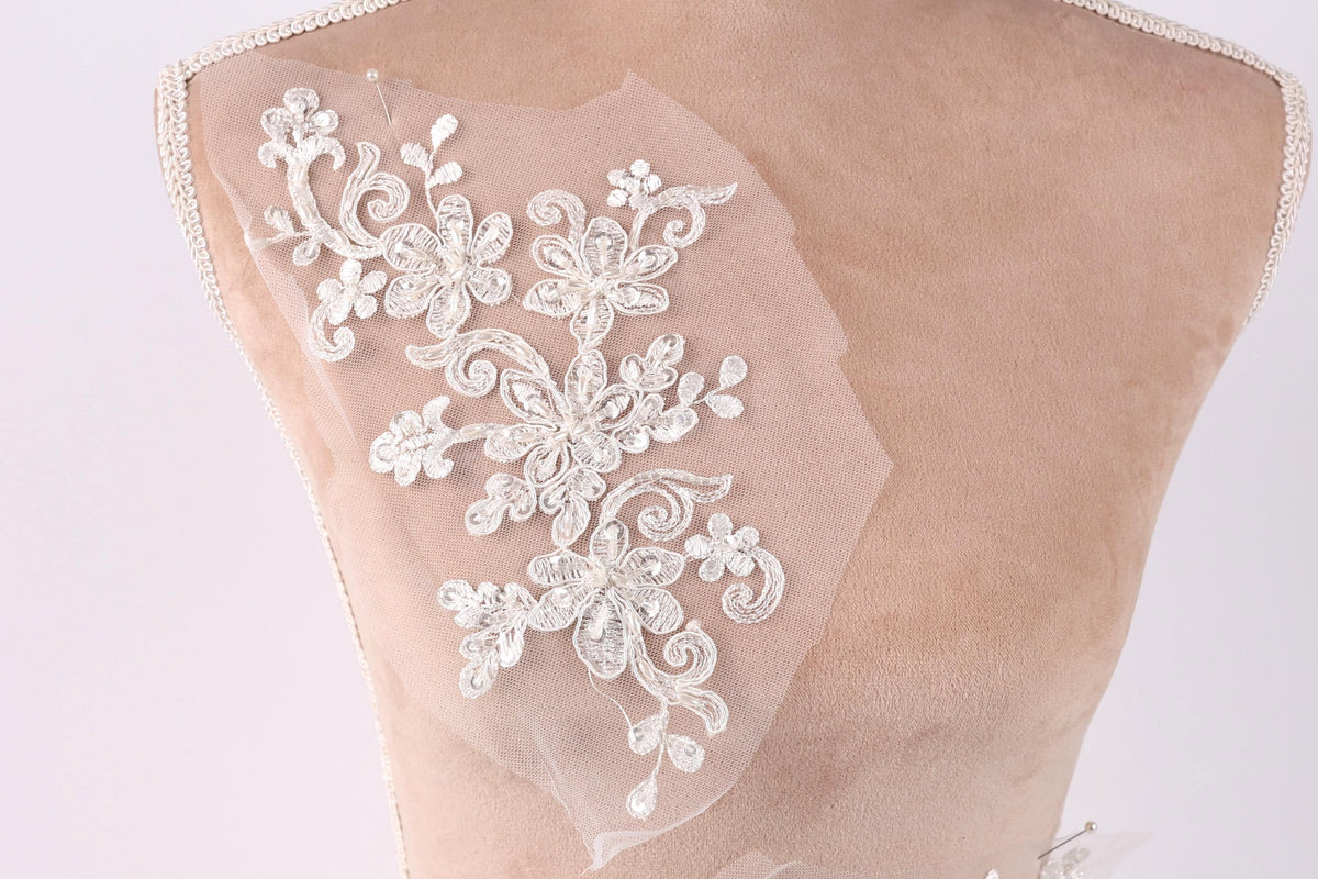 A close-up of a mannequin torso with a delicate, intricate white lace embroidery on the back.
