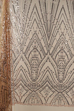 a close-up view of a fabric with a repeating pattern of black and gold sequin designs. The pattern consists of various geometric shapes and lines, creating a visually striking and intricate design. The fabric appears to be a piece of clothing or textile, with the intricate pattern suggesting a high level of craftsmanship and attention to detail.