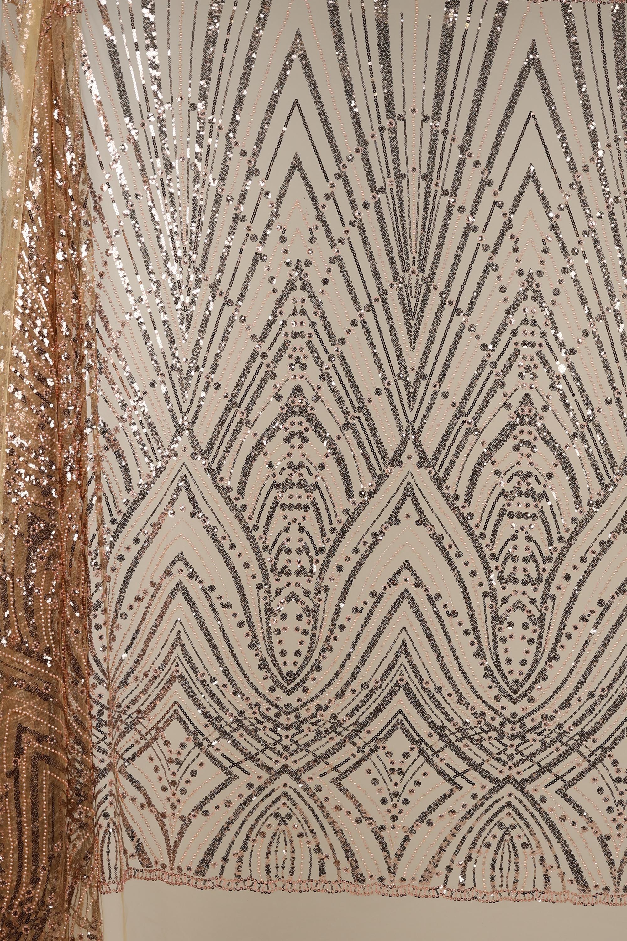 a close-up view of a fabric with a repeating pattern of black and gold sequin designs. The pattern consists of various geometric shapes and lines, creating a visually striking and intricate design. The fabric appears to be a piece of clothing or textile, with the intricate pattern suggesting a high level of craftsmanship and attention to detail.
