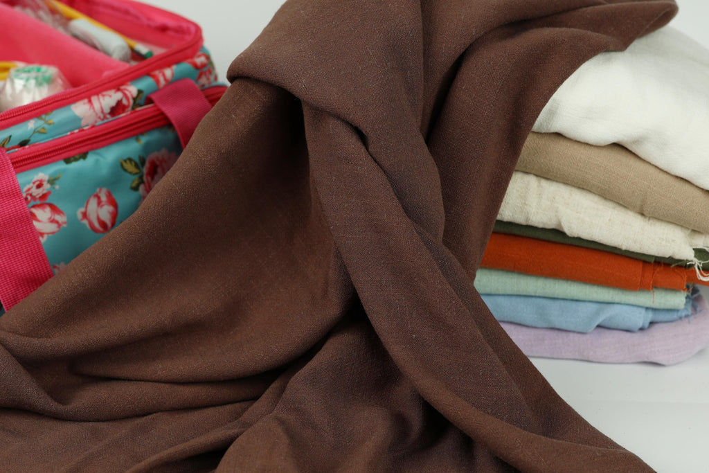 A pile of folded clothes, including a brown fabric, is placed next to a colorful bag with a floral pattern.