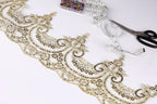 a close-up view of a decorative gold lace trim with intricate floral patterns, along with a pair of scissors and a measuring tape on a white background.