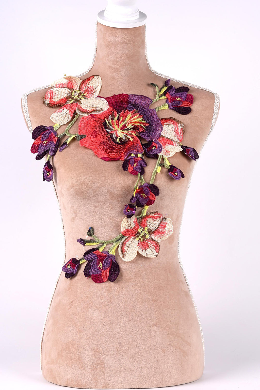 A mannequin bust is adorned with a vibrant floral embroidery, featuring a variety of colorful flowers including red, purple, and white blooms.
