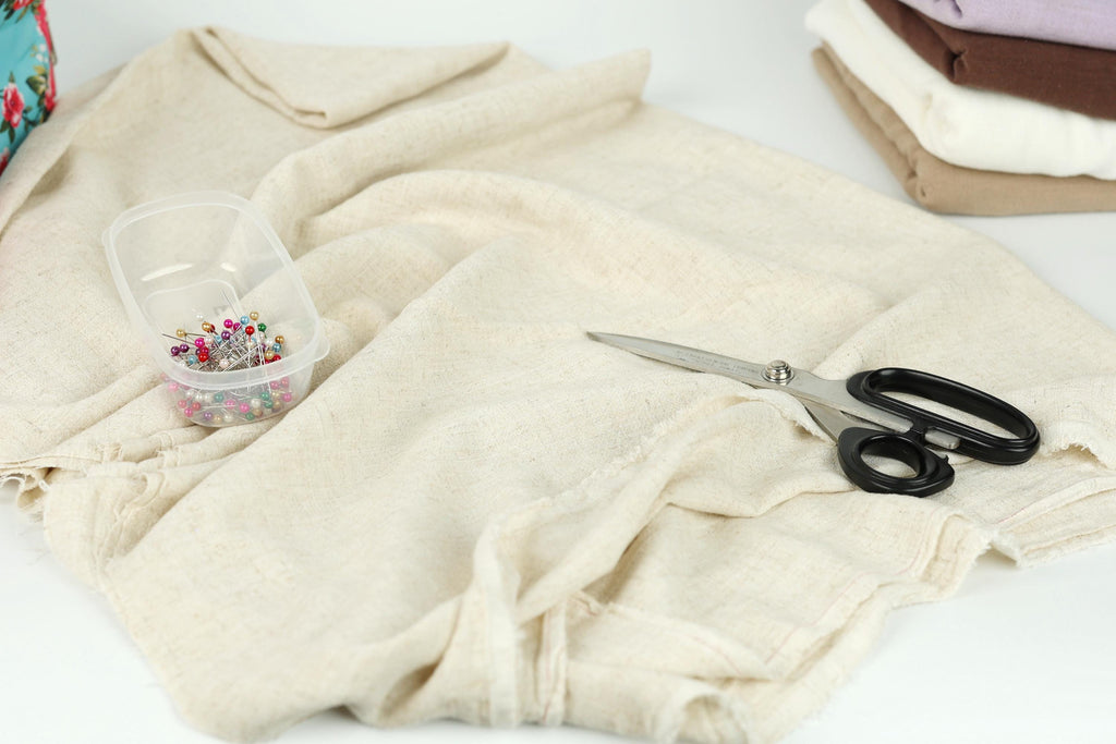 a sewing kit with a pair of scissors, pins, and a clear container filled with colorful pins on a white surface.
