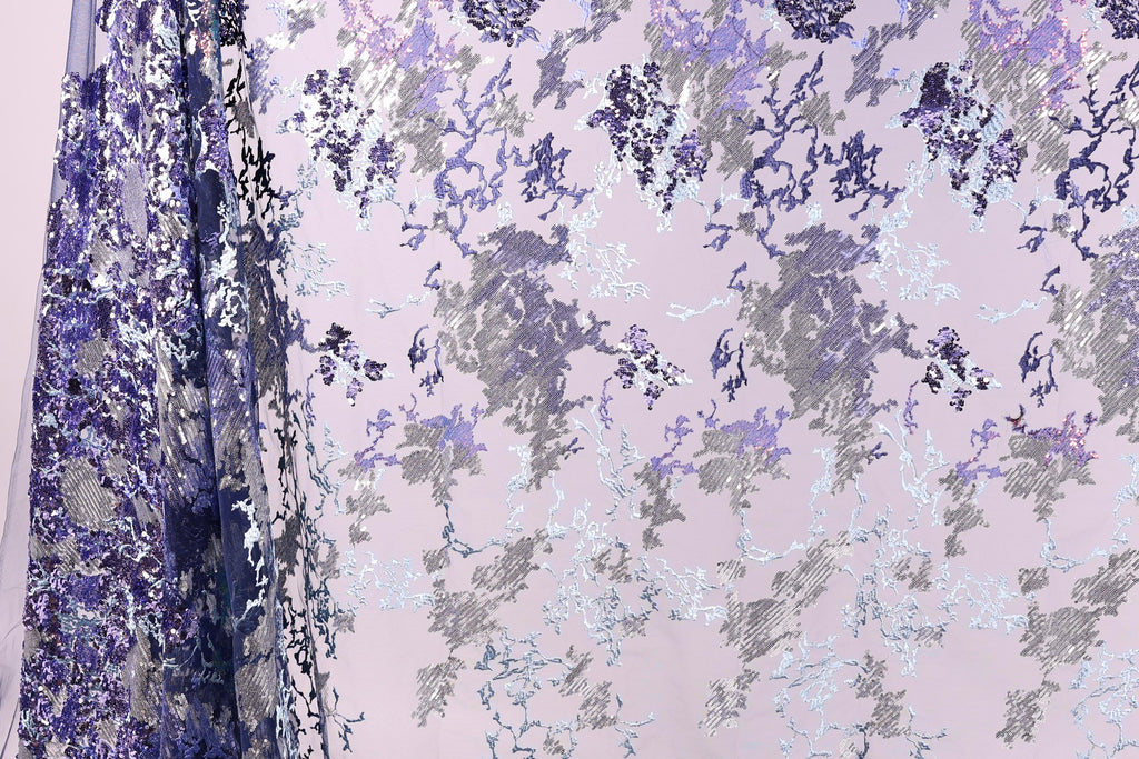 a fabric with a floral pattern in shades of purple and gray, with some white accents. The fabric appears to be a sheer or sheer-like material, with a delicate and intricate design.